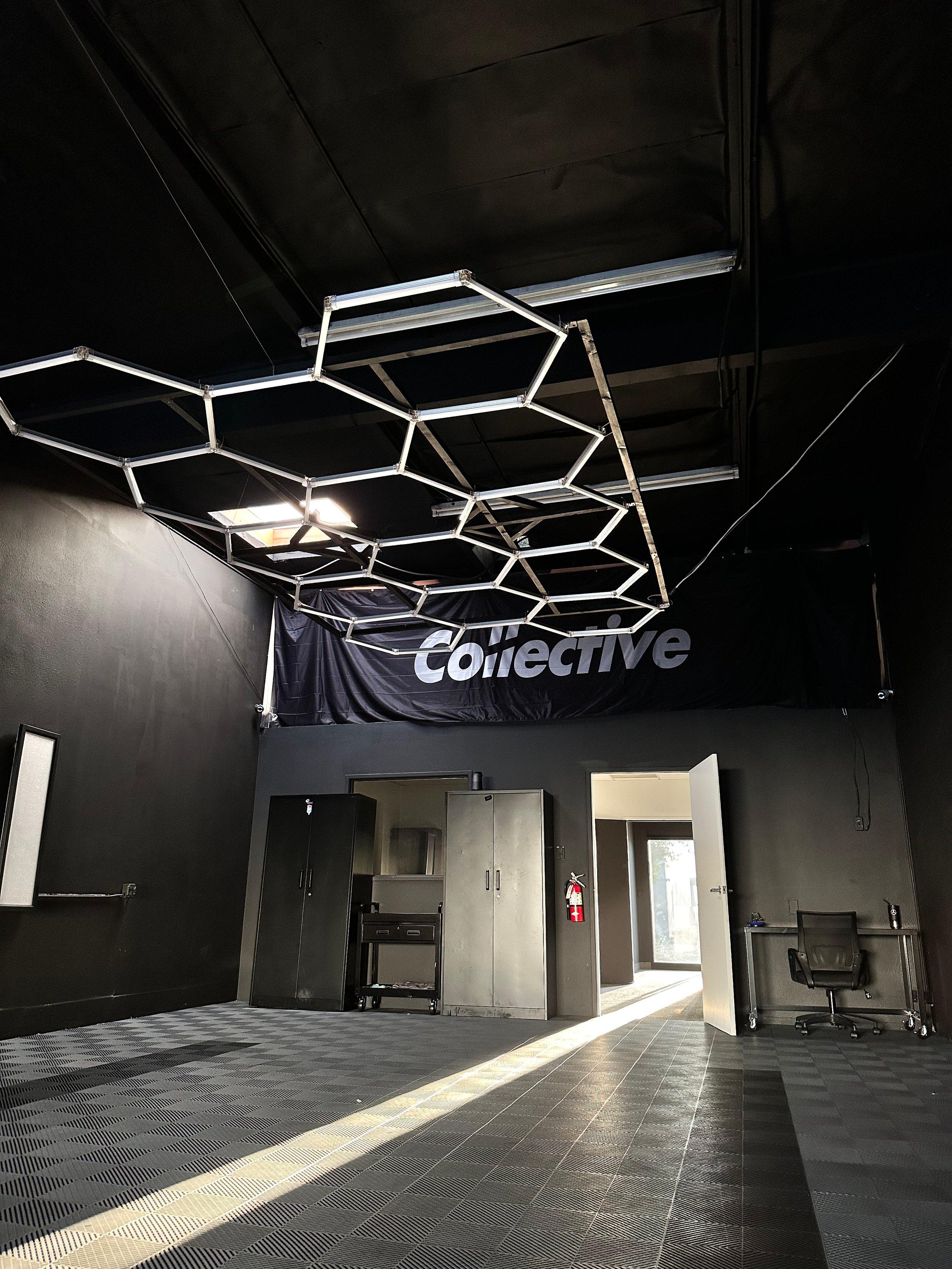 Empty shop bay with a hexagon ceiling light grid, the Collective banner, tool cabinets and grey interlocking floor tiles