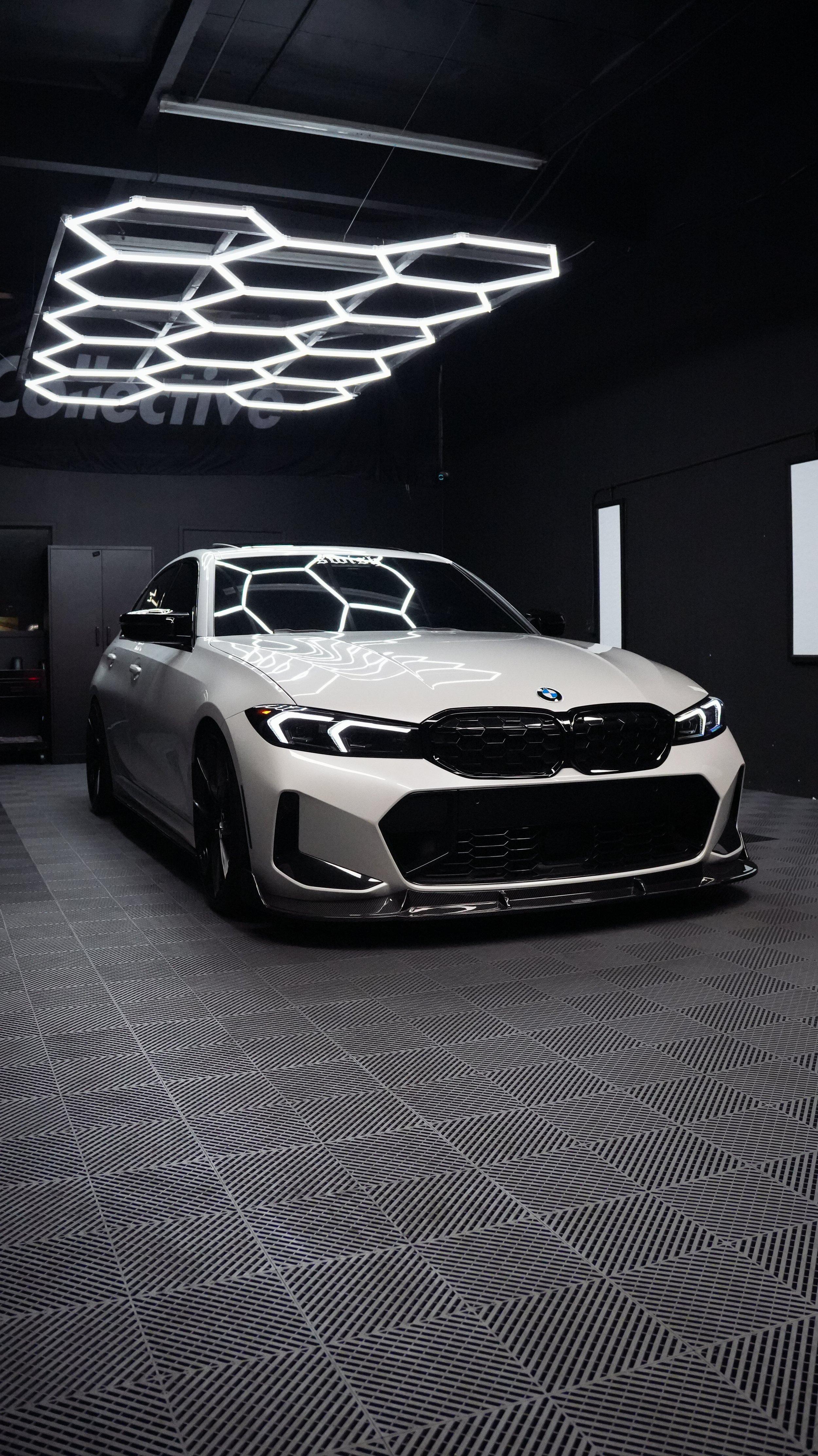 White BMW 3 Series with M Performance front splitter and hex light reflections on the hood inside the shop bay