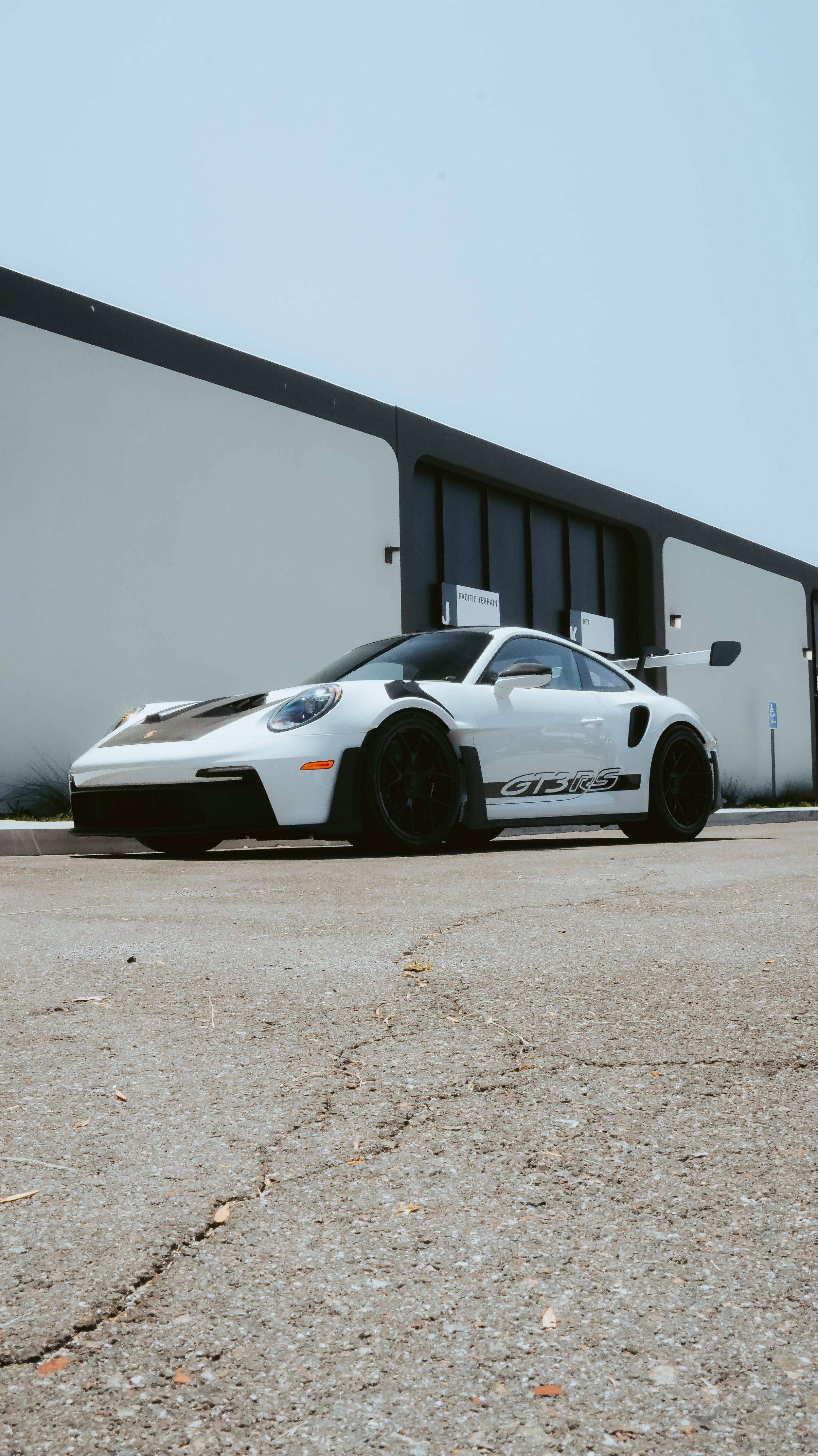 White Porsche 911 GT3 RS with black wheels parked outside the shop, shot from low on the asphalt