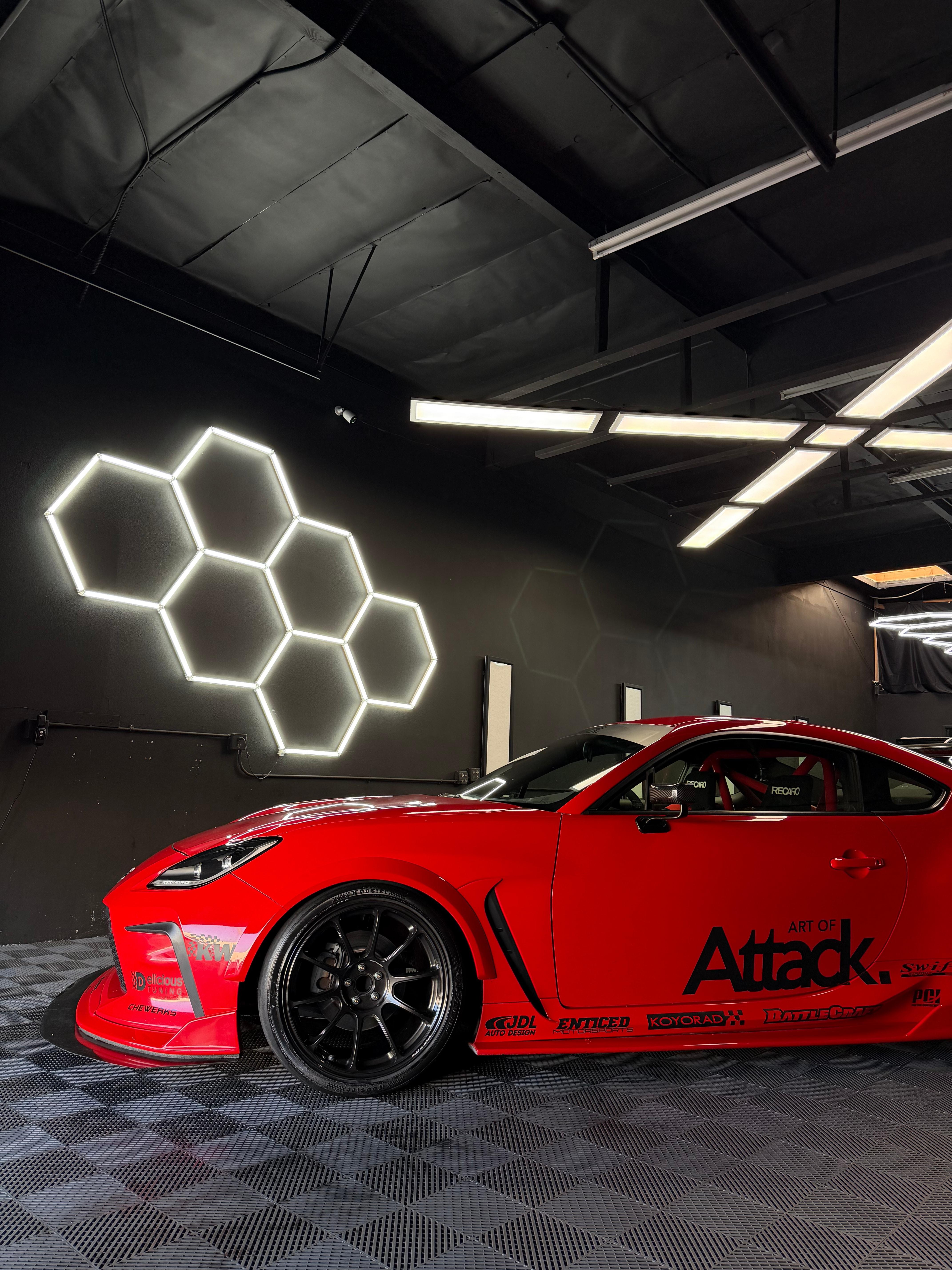 Red Toyota GR86 with Art of Attack livery and roll cage beside the hex wall light