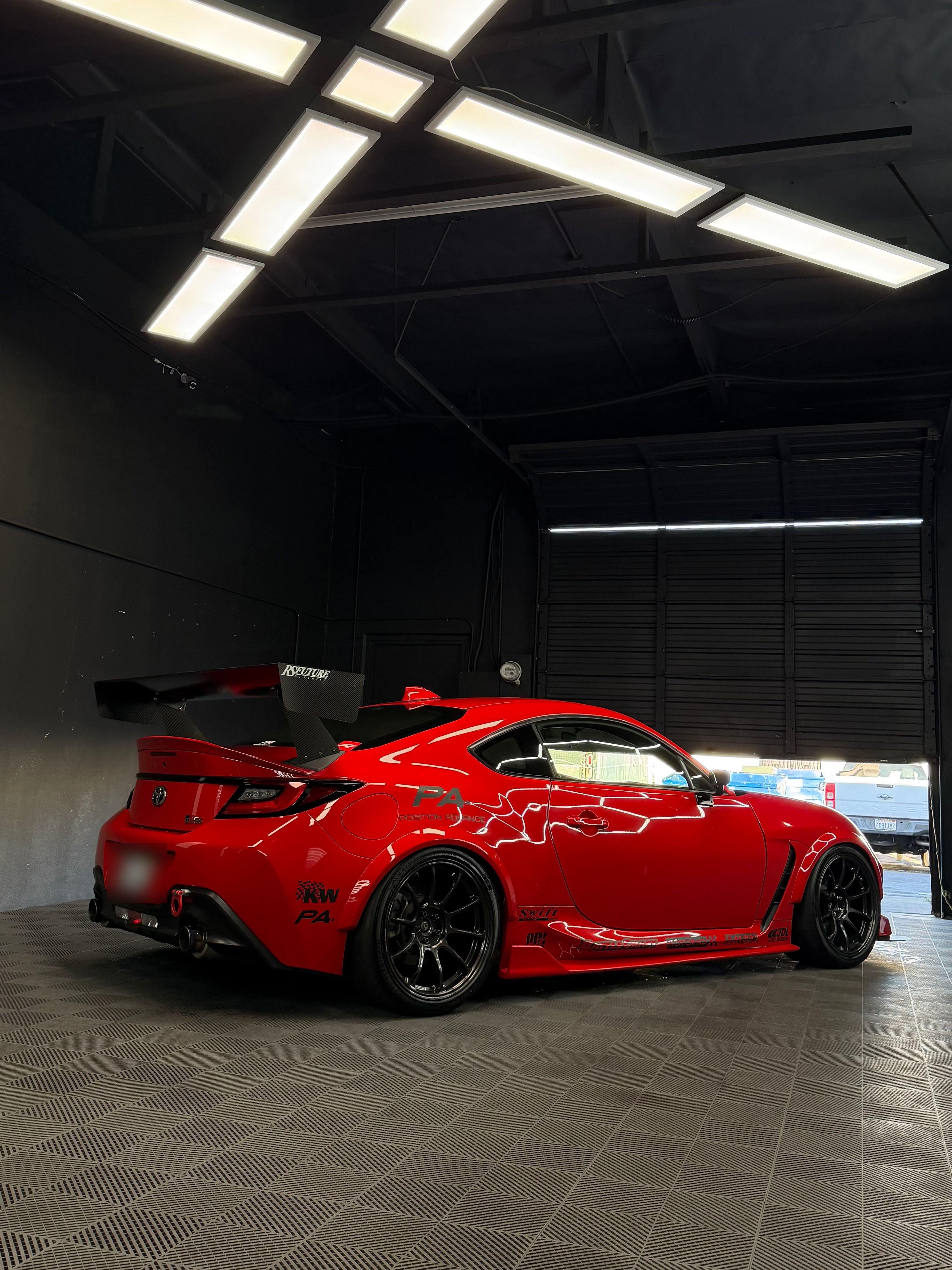 Red Toyota GR86 with a big rear wing parked in the open bay door of the studio