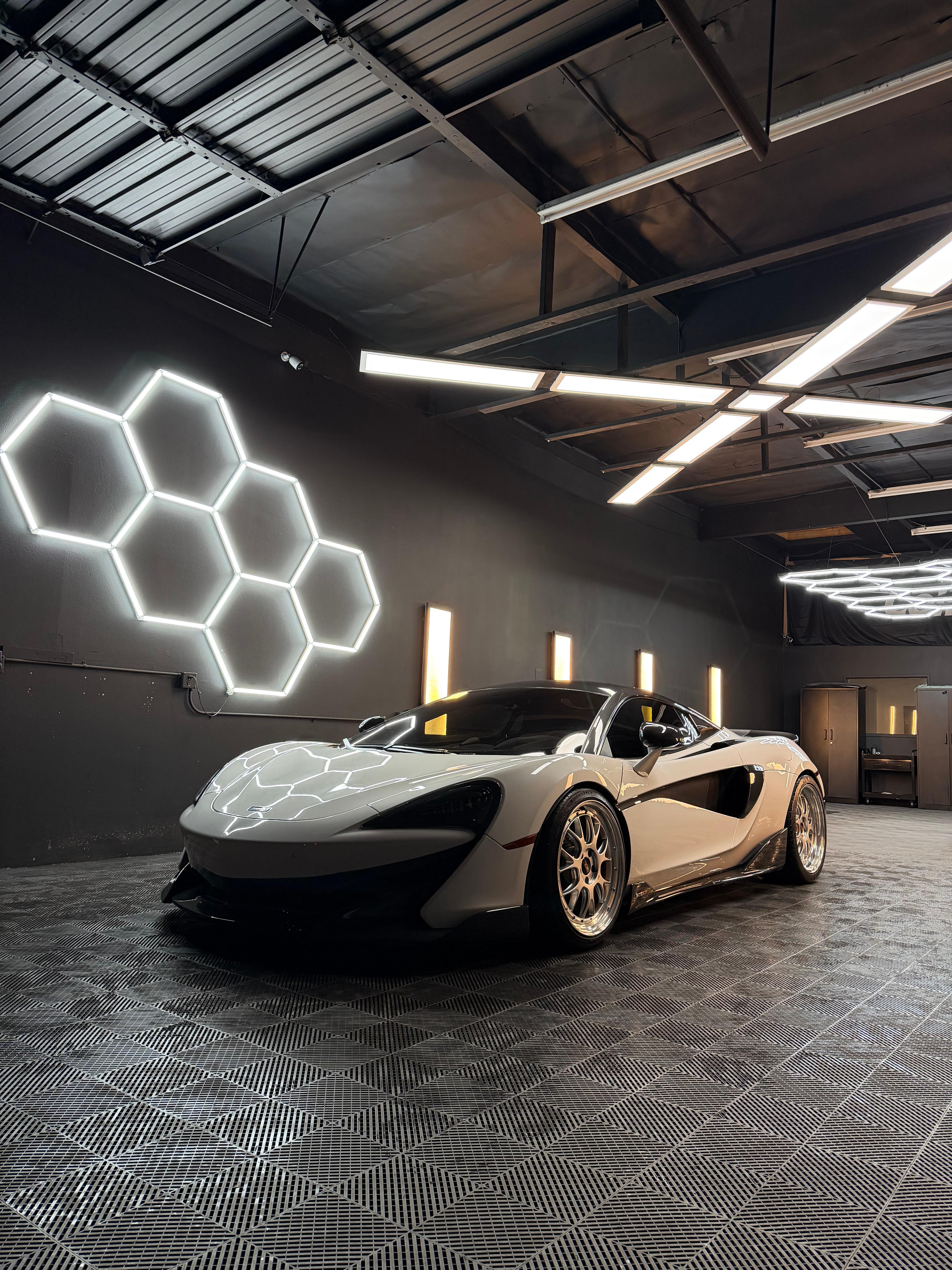 White McLaren 570S with gold wheels under the hex wall light and bar lights in the bay