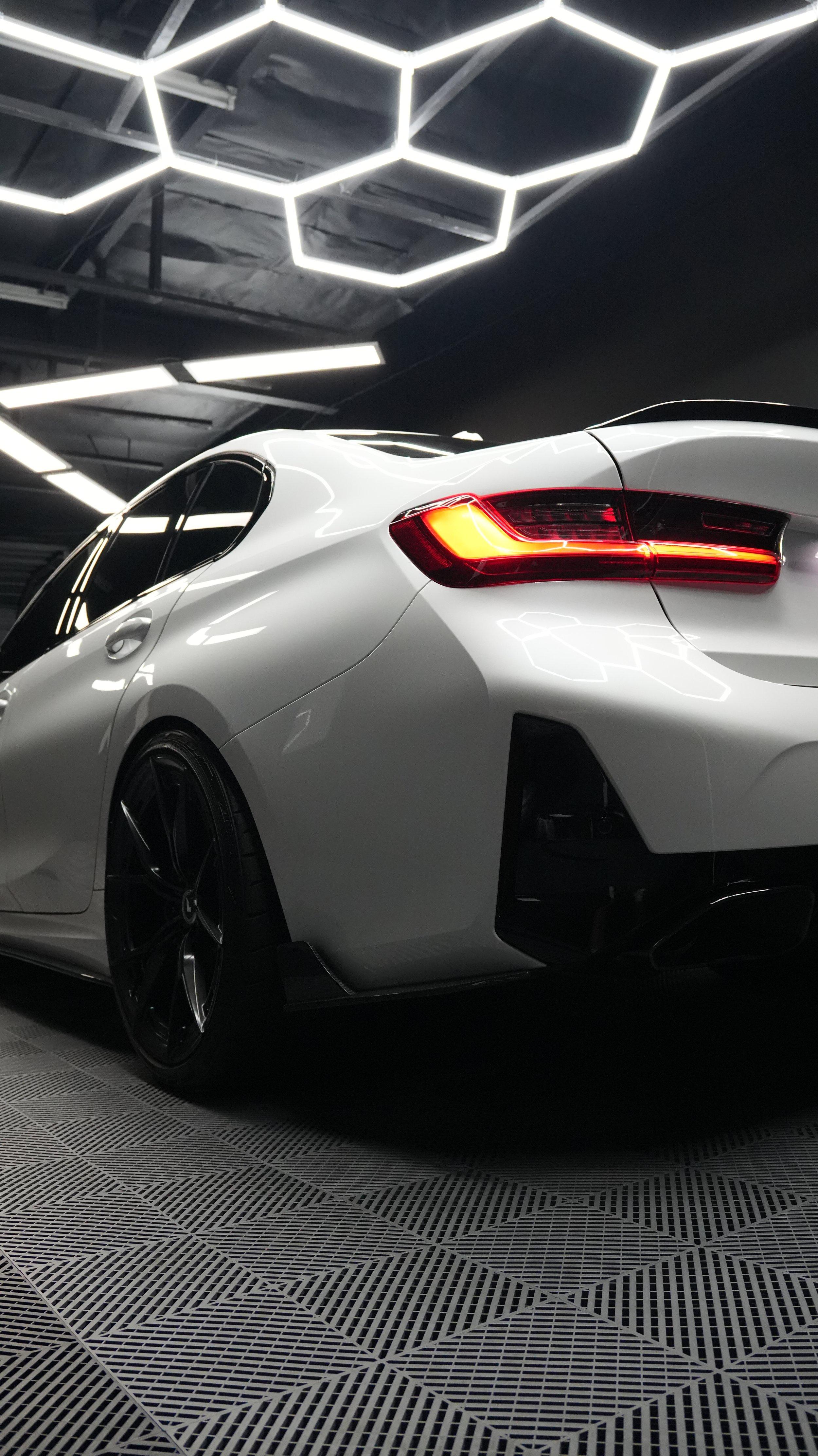 White BMW rear quarter with gloss black wheels under hexagon ceiling lights in the studio