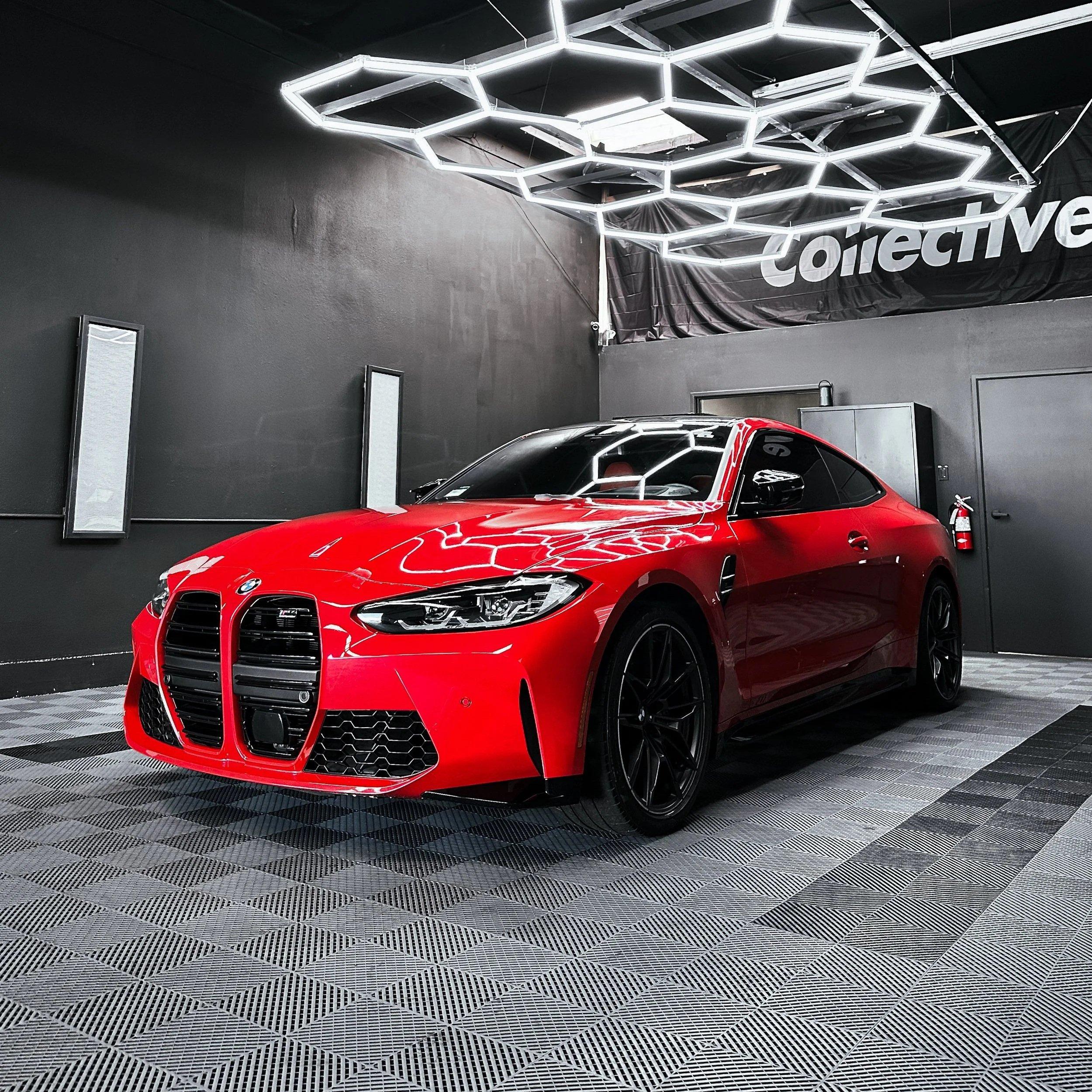 Red BMW M4 parked under hexagon ceiling lights inside the Collective Detailing studio