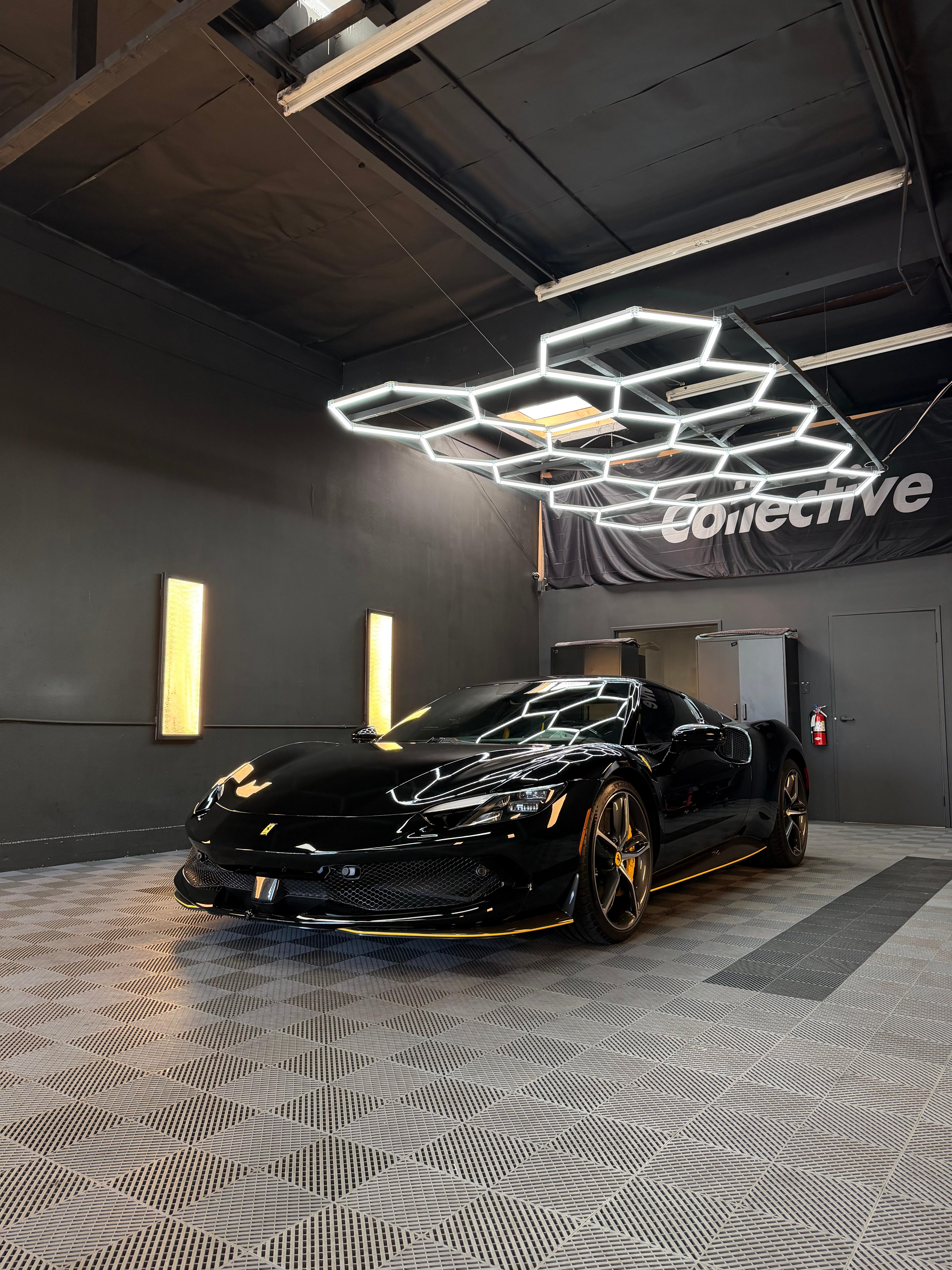 Gloss black Ferrari with bronze wheels beneath the Collective banner and hexagon lights